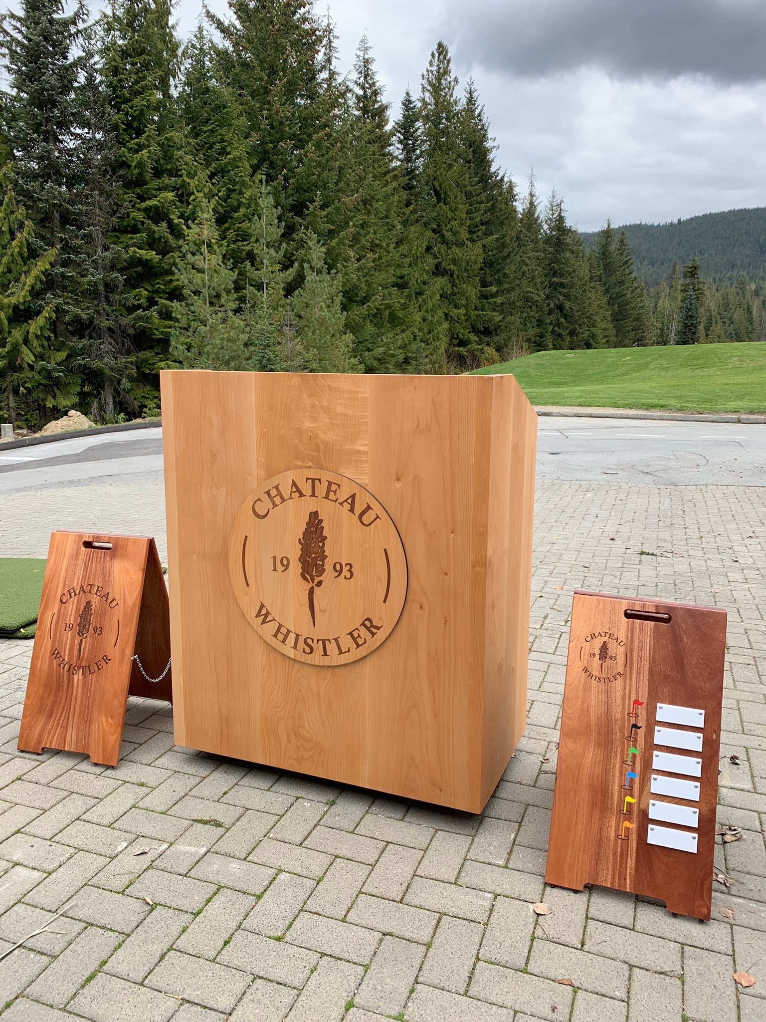 Handcrafted wooden starter station sign with Chateau Whistler 1993 logo, flanked by two smaller A-frame yardage signs.