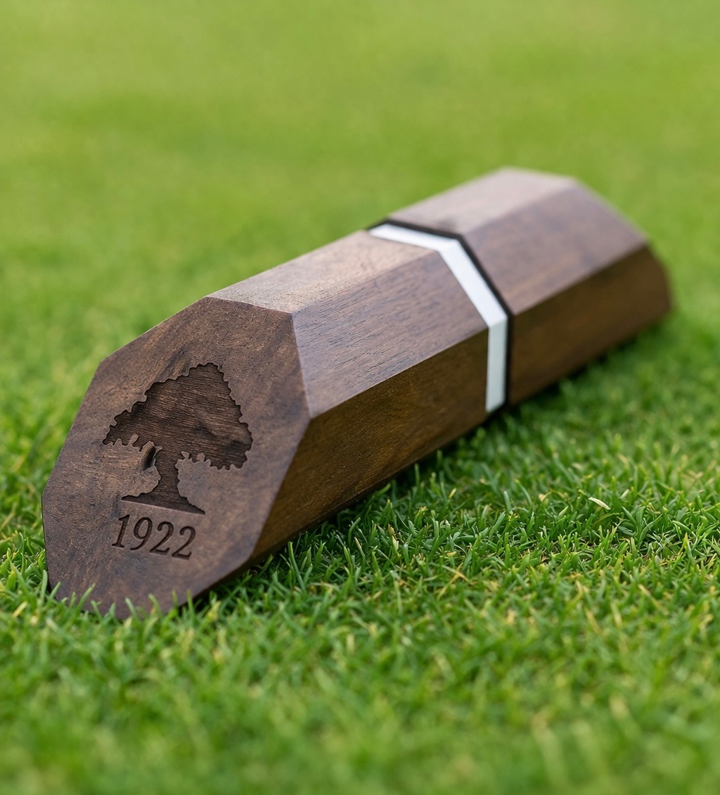 Dark walnut hexagonal tee marker with white inlay stripe, engraved tree logo and 1922 date mark, on turf.
