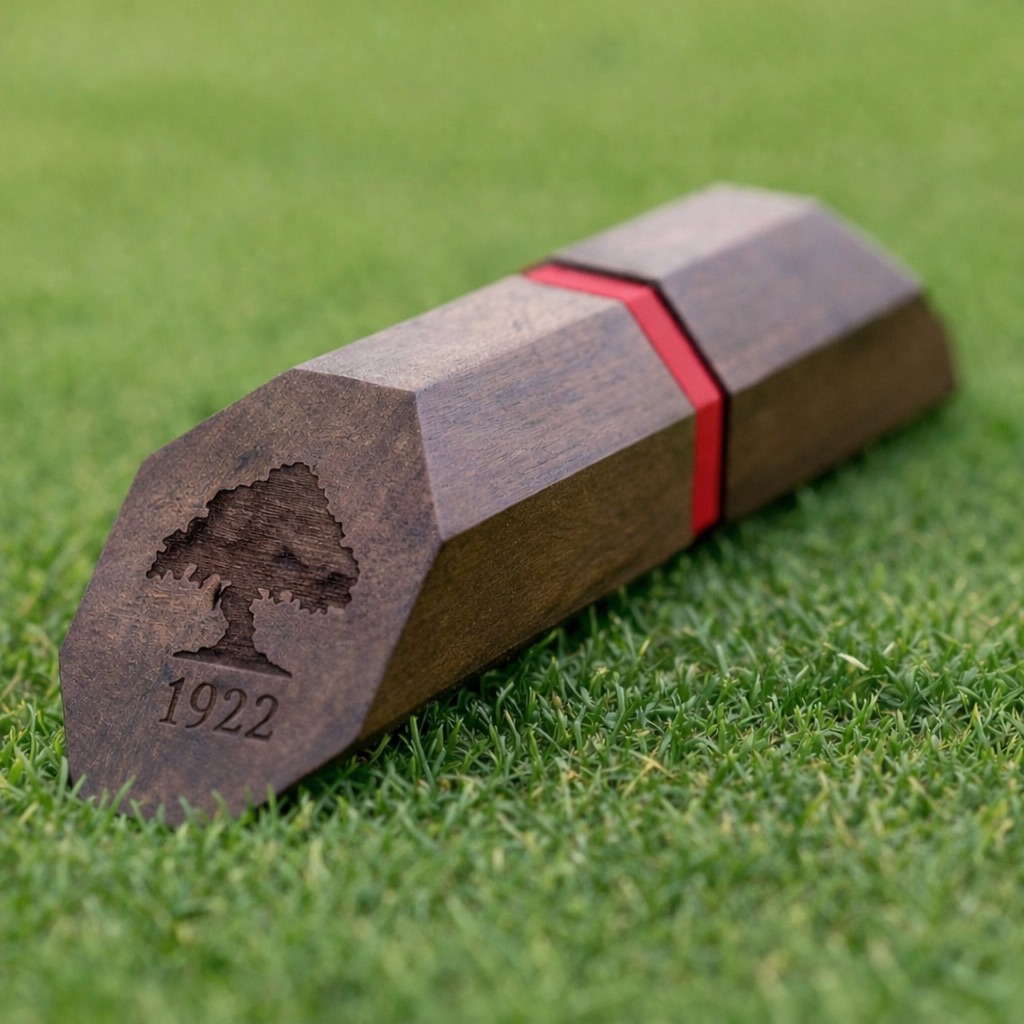 Dark walnut hexagonal tee marker with red inlay stripe, engraved tree logo and 1922 date mark, on turf.