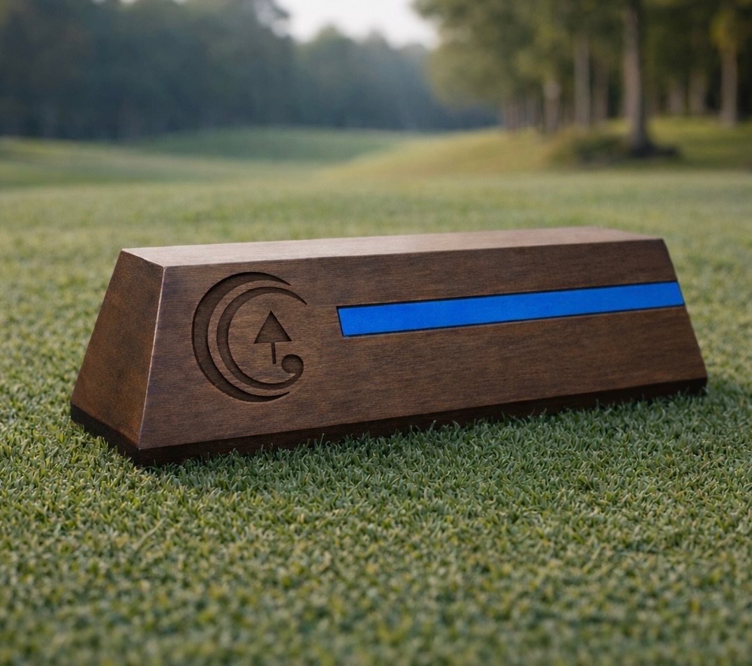 Walnut rectangular tee marker with blue inlay stripe on a fairway, trees in the background.