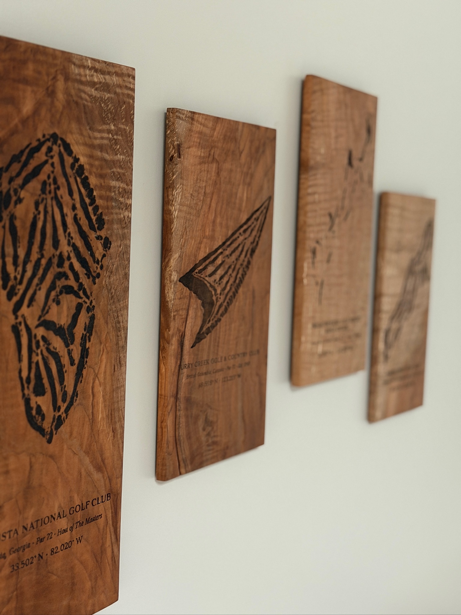 Four course map plaques mounted on a wall, including Augusta National, engraved on raw and figured wood.