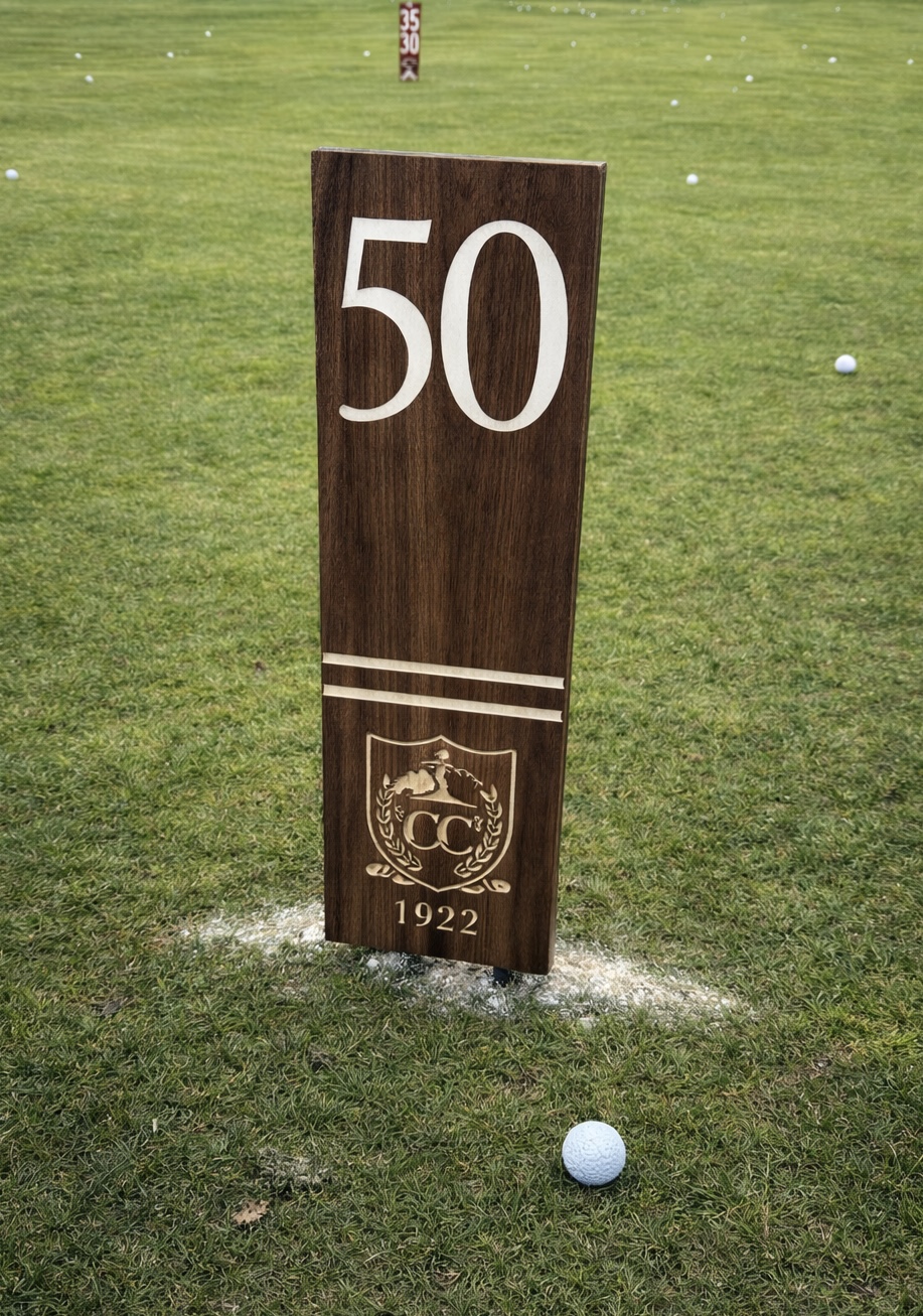 Walnut yardage marker with engraved 50-yard distance, club crest and 1922 date mark, on the driving range.